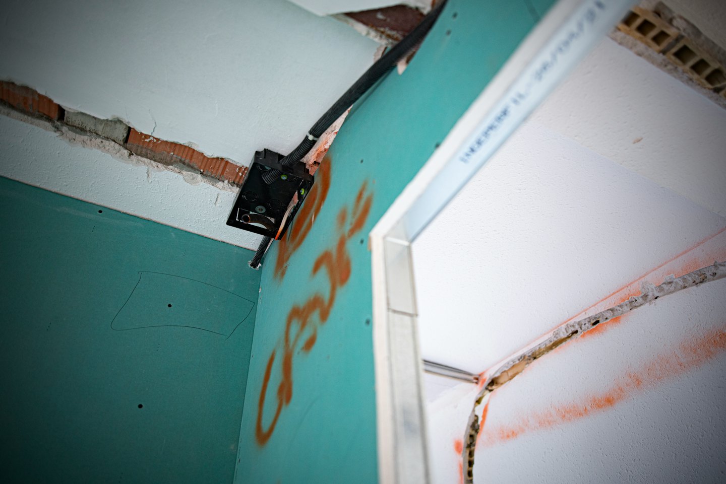 Grüne Gipskartonwand mit Elektroleitungen und rotem Ziegelakzent.